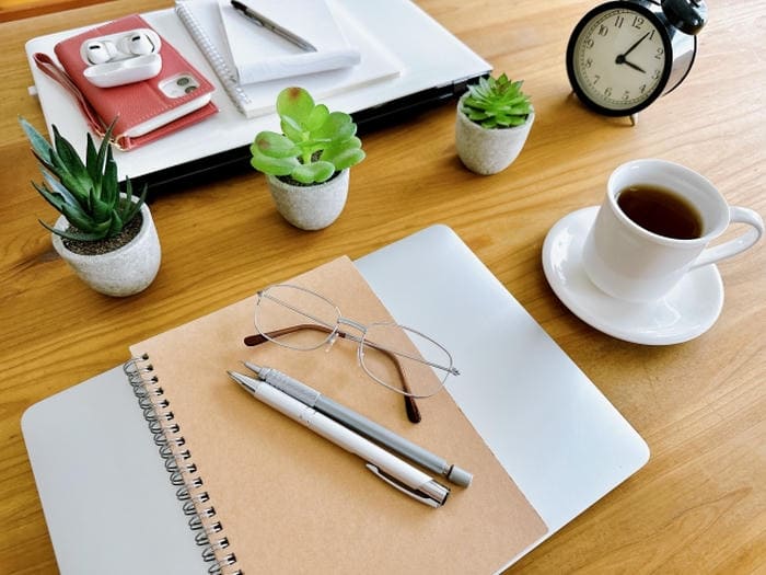机の上にノートとペン、眼鏡、コーヒーが置かれた勉強の合間のデスク