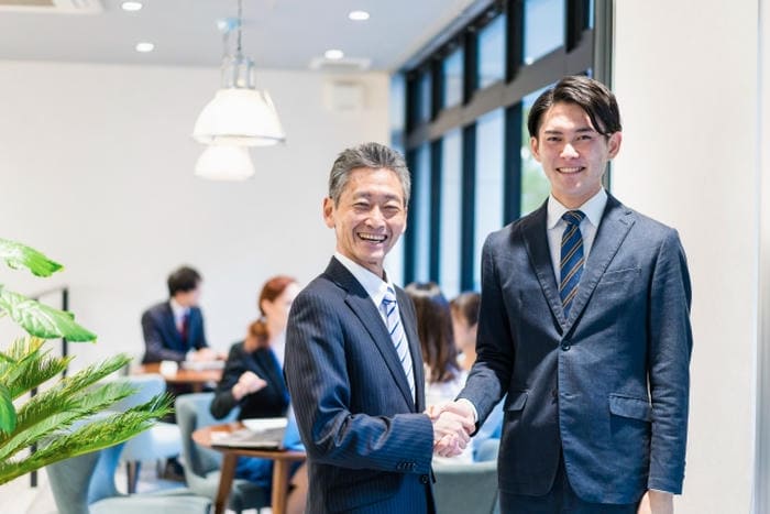 オフィスでスーツ姿の男性2人が笑顔で握手をしている様子