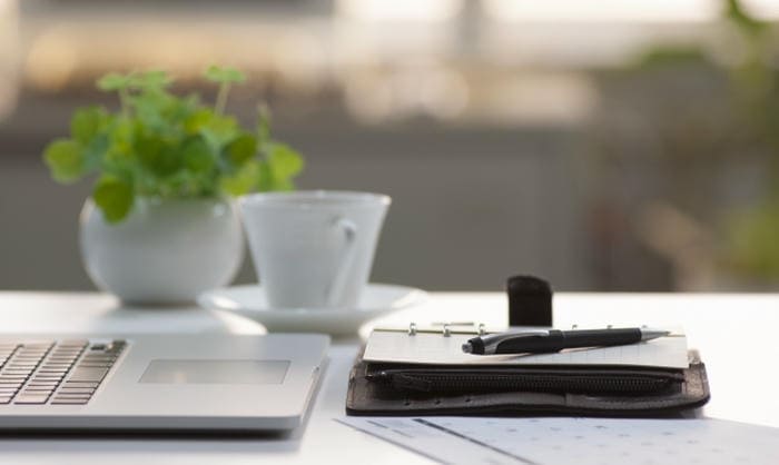 ノートパソコンと手帳、ペン、コーヒーカップが置かれた整ったデスク