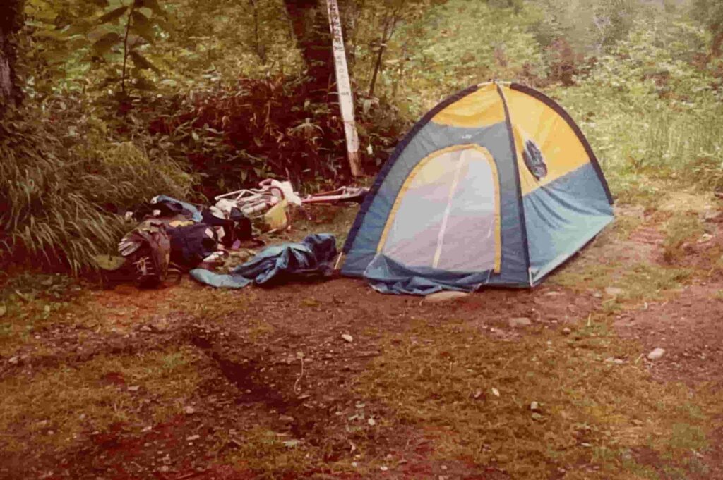 知床半島の羅臼キャンプ場で設営された、黄色と青色のドーム型テント。傍らには自転車旅の荷物が置かれ、周囲を深い緑に囲まれた、静かな野営の情景を捉えた写真。