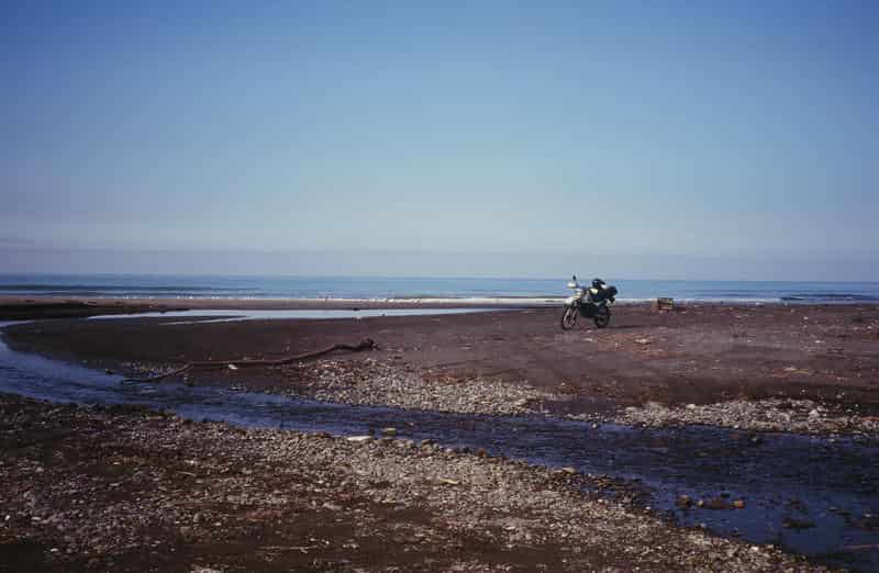 海岸の砂地に停められたオフロードバイクと遠くに広がる海