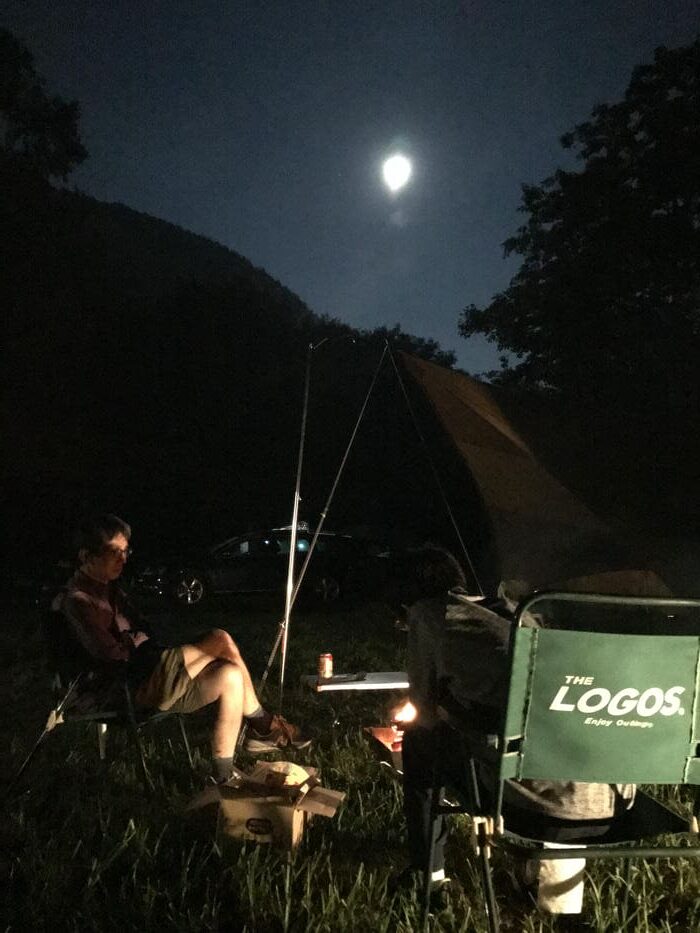 キャンプ場の夜、月明かりと焚き火のそばで静かに過ごす親子の様子